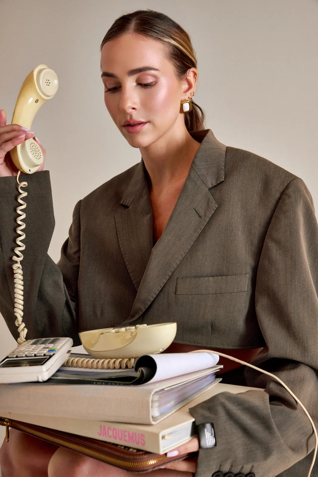Éditorial mode, femme en blazer avec un téléphone vintage, fond papier taupe